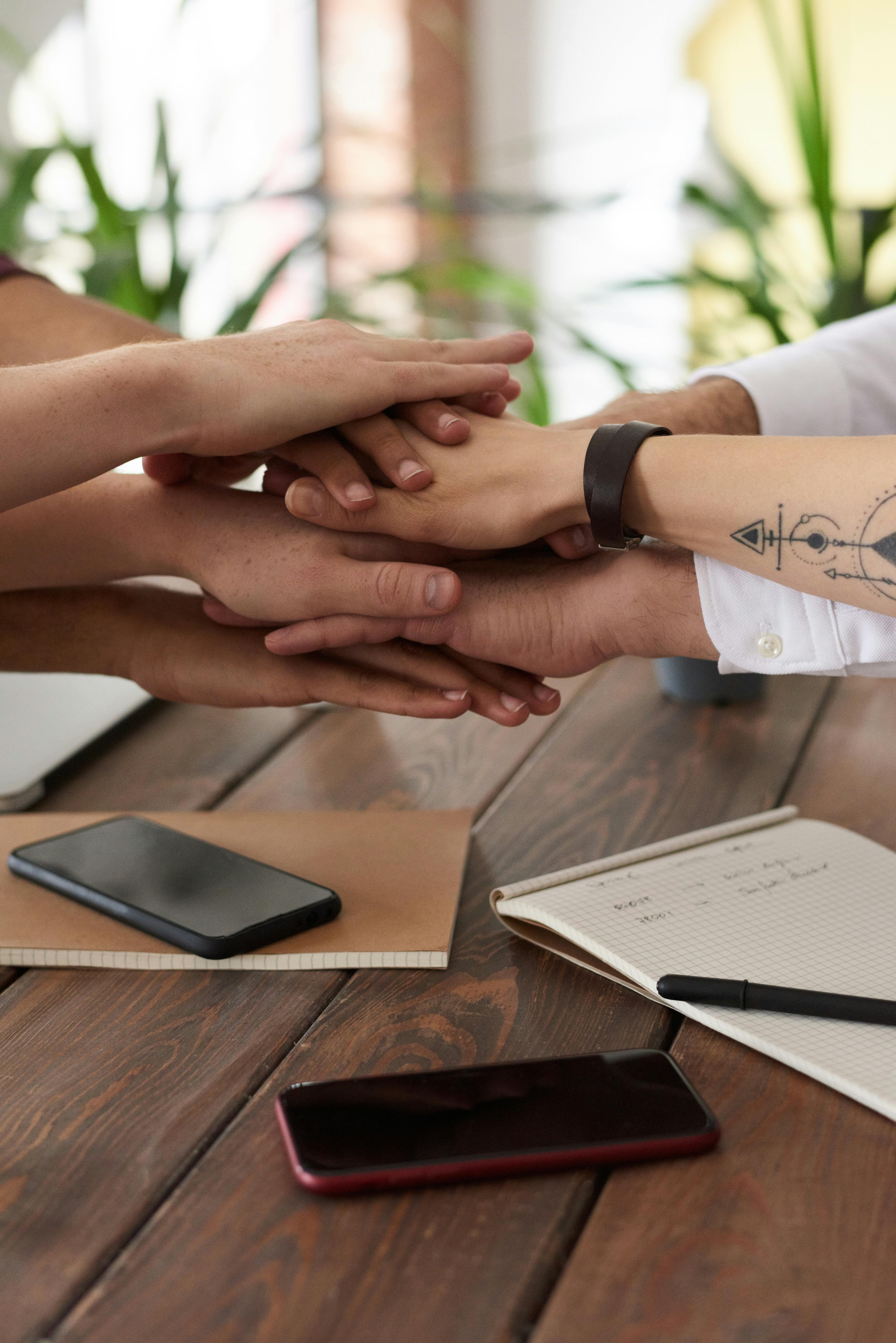 Team hands together over a boardroom table with notebooks and phones